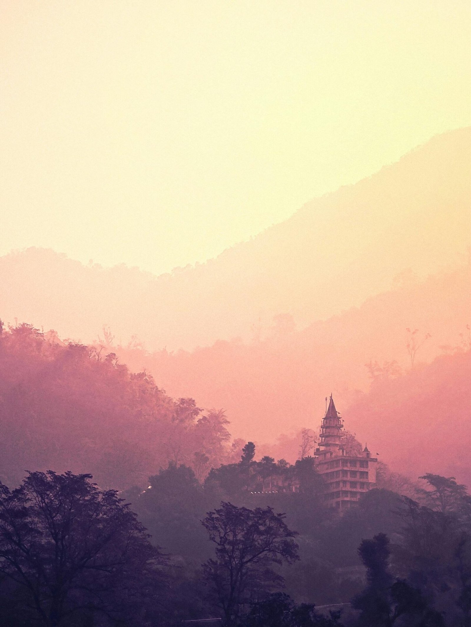 A tranquil view of Rishikesh mountains and temple enveloped in pink hues at sunrise.